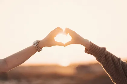 Dos manos formando un corazón a contraluz durante el atardecer