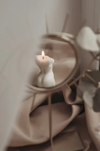 Vela con forma de cuerpo encendida frente a un espejo de tocador